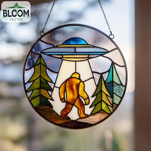 May include: Round stained glass panel featuring a UFO hovering over a Bigfoot figure. The design includes trees and a night sky, with a metal frame and hanging chain. The Bloom Vector logo is in the upper left corner.