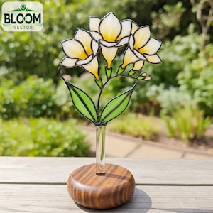 May include: A stained glass flower sculpture with yellow and white petals, green leaves, and a clear glass stem. The flower is set in a round, wooden base. The Bloom Vector logo is in the upper left corner.
