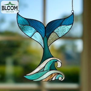 May include: A stained glass whale tail suncatcher in shades of blue, teal, and white. The design features a whale tail above stylized waves. The suncatcher is suspended by a chain and includes the text "BLOOM VECTOR".