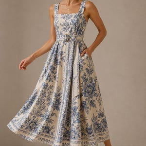Peut inclure: Une robe midi sans manches en tissu crème ornée d'un motif floral bleu. La robe présente une encolure carrée, un corsage ajusté et une jupe évasée avec une ceinture en tissu assortie dotée d'une boucle circulaire à la taille.