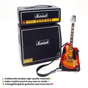 May include: Miniature black Marshall amplifier stack with a matching electric guitar. The amplifier has the Marshall logo and JCM 800 LEAD SERIES text. The guitar is red and orange with a black strap. A thoughtful gift for guitarists.