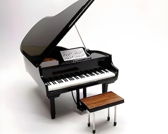 Peut inclure: Un piano à queue noir miniature avec une finition brillante, avec des touches blanches et noires, un pupitre avec des partitions et un banc assorti. Le couvercle du piano est ouvert, et le banc a un dessus en bois et des pieds argentés. Le piano est sur fond blanc.