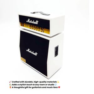 Könnte beinhalten: Ein weißer Marshall-Verstärkerstapel mit schwarzen Lautsprecherabdeckungen. Der Verstärker hat goldene Knöpfe und das Marshall-Logo in Weiß. Der Text "JCM 800" ist sichtbar. Oben befindet sich ein schwarzer Griff.