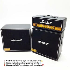 Könnte beinhalten: Schwarzes Marshall-Verstärker-Set mit weißem Marshall-Logo. Das Set enthält eine Lautsprecherbox und einen Verstärkerkopf. Der Verstärkerkopf hat einen Griff und goldfarbene Akzente. Der Text "JCM 800 LEAD 1960" ist sichtbar.