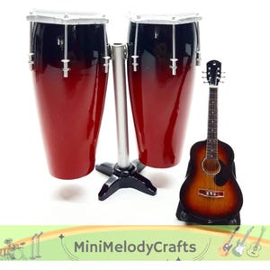 May include: A set of miniature musical instruments. Features two red and black conga drums with a silver stand and a brown and tan acoustic guitar. The guitar is on a black stand. The text "MiniMelodyCrafts" is at the bottom.