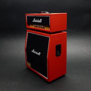 Puede incluir: Un amplificador Marshall rojo con una caja de altavoz negra. El cabezal del amplificador está en la parte superior, con perillas y el logotipo de Marshall. La caja del altavoz tiene el logotipo de Marshall y una cubierta de altavoz negra.