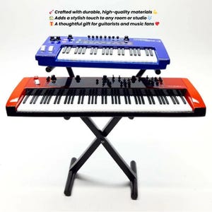 Op de afbeelding: Twee speelgoed synthesizers, één blauw en één rood, zijn op een zwarte standaard gestapeld. De keyboards hebben witte toetsen en zwarte accenten. De afbeelding bevat de tekst "Gemaakt met duurzame, hoogwaardige materialen" en "Een attent cadeau voor gitaristen en muziekliefhebbers."