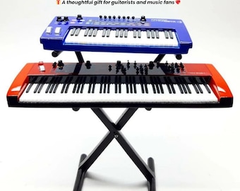 May include: Two toy synthesizers, one blue and one red, are stacked on a black stand. The keyboards have white keys and black accents. The image includes text that says "Crafted with durable, high-quality materials" and "A thoughtful gift for guitarists and music fans."
