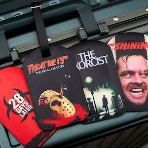 May include: Four luggage tags with horror film designs. The tags show the titles "28 Days Later", "Friday the 13th", "The Exorcist", and "The Shining". Each tag has a black strap for attachment.