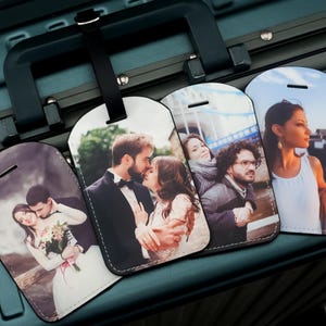 Op de afbeelding: Een verzameling gepersonaliseerde bagagelabels met verschillende foto's. De labels zijn rechthoekig met afgeronde hoeken en een zwarte rand. Elke label toont een andere afbeelding van stellen en individuen. De labels zijn bevestigd aan een tealkleurige kofferhandgreep.