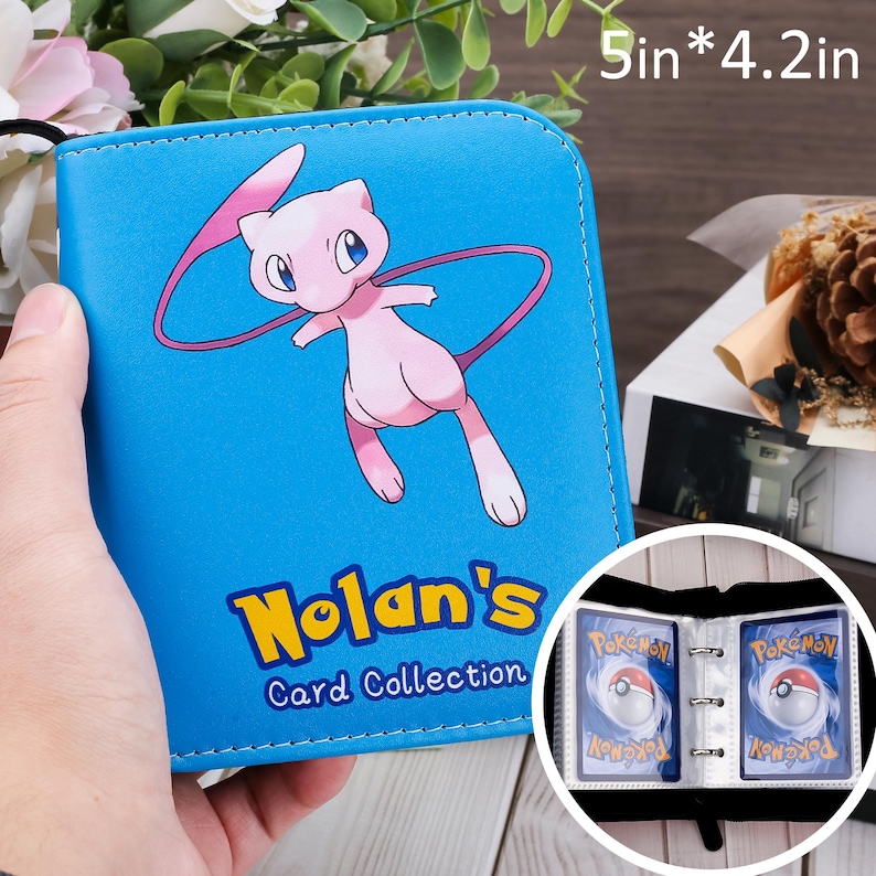May include: A blue card binder with a pink cartoon character and the text "Nolan's Card Collection." The binder is 5 inches by 4.2 inches and has clear pockets for storing cards.
