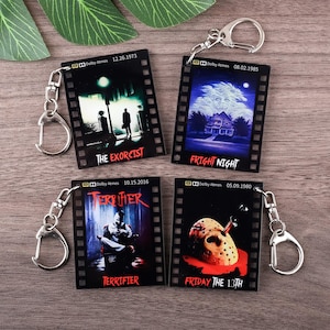 May include: Four black keychains featuring horror movie posters: "The Exorcist", "Fright Night", "Terrifier", and "Friday the 13th". Each keychain has a silver metal clasp and a film strip design with movie titles and dates.