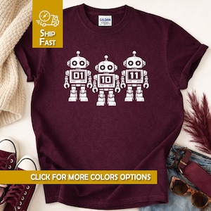 Könnte beinhalten: Burgunderfarbenes T-Shirt mit drei weißen Roboter-Illustrationen, die die Zahlen 01, 10 und 11 zeigen. Das Shirt hat einen Rundhalsausschnitt und kurze Ärmel. Der Text "CLICK FOR MORE COLORS OPTIONS" ist unten im Bild zu sehen.