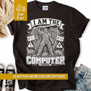 May include: A black short-sleeved t-shirt featuring a white graphic print of a robotic figure in armor holding a sword. The text reads I AM THE COMPUTER, with additional labels including ERROR, SYSTEM FAILURE, and warning icons with a skull.