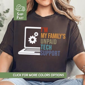 May include: Dark brown t-shirt with the text "I'M MY FAMILY'S UNPAID TECH SUPPORT" in various colors. A white laptop graphic with gear icons is on the front. The shirt also has a "Ship Fast" graphic.