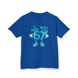 Pu&ograve; includere: T-shirt blu reale con la scritta "I WAS 67 NOW I'M" sopra un numero 67 in stile cartone animato. Il numero 67 ha braccia, gambe e scarpe, con i pollici in su. Un cappello da festa &egrave; in cima al numero 7.