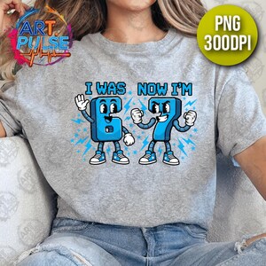 May include: A light gray t-shirt featuring a cartoon graphic of the numbers 6 and 7 with faces, arms, and legs. The text "I WAS NOW I'M" is above the numbers. The numbers are blue with white accents and lightning bolt details.