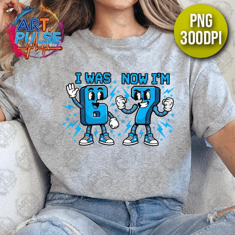 May include: A light gray t-shirt featuring a cartoon graphic of the numbers 6 and 7 with faces, arms, and legs. The text "I WAS NOW I'M" is above the numbers. The numbers are blue with white accents and lightning bolt details.