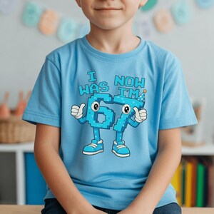 Pu&ograve; includere: Una maglietta azzurra con la scritta "I WAS 6, NOW I'M 7". I numeri 6 e 7 sono figure antropomorfe con braccia, gambe e scarpe. Il numero 7 indossa un cappello da festa. La maglietta &egrave; per un bambino.