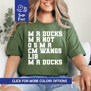 May include: Olive green t-shirt with white text: "MR DUCKS MR NOT OSMR CM WANGS LIB MR DUCKS." The shirt also has the text "CLICK FOR MORE COLORS OPTIONS" and a "SHIP FAST" graphic.