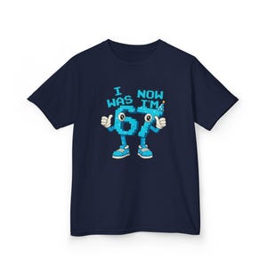 Pu&ograve; includere: T-shirt blu navy con una grafica del numero 67 come un personaggio dei cartoni animati con braccia, gambe e scarpe. Il testo sopra il numero recita "I WAS NOW I'M". Il personaggio &egrave; blu con dettagli bianchi e un cappello da festa.