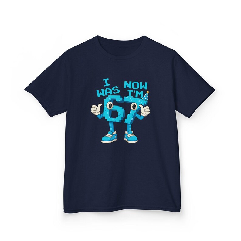 Pu&ograve; includere: T-shirt blu navy con una grafica del numero 67 come un personaggio dei cartoni animati con braccia, gambe e scarpe. Il testo sopra il numero recita "I WAS NOW I'M". Il personaggio &egrave; blu con dettagli bianchi e un cappello da festa.