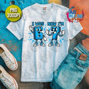 May include: White t-shirt with the text "I WAS NOW I'M" and cartoon-style numbers 6 and 7. The numbers are blue with white accents and are depicted with arms, legs, and shoes. A pair of jeans and sneakers are also in the image.