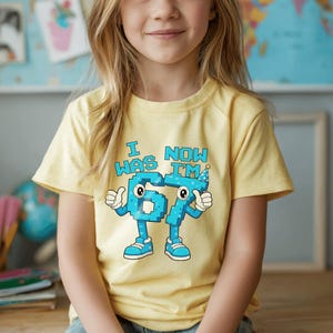Pu&ograve; includere: Una maglietta gialla con la scritta "I WAS 67 NOW I'M" in blu. I numeri 6 e 7 sono disegnati come personaggi dei cartoni animati con occhi, braccia, gambe e scarpe. Il numero 7 indossa un cappello da festa.