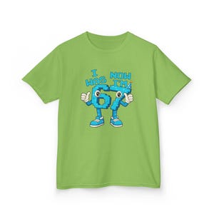 Pu&ograve; includere: T-shirt verde lime con la scritta "I WAS 67 NOW I'M" e il numero 67 disegnato come un personaggio dei cartoni animati. Il numero &egrave; blu con dettagli bianchi, pollice in su e un cappello da festa.