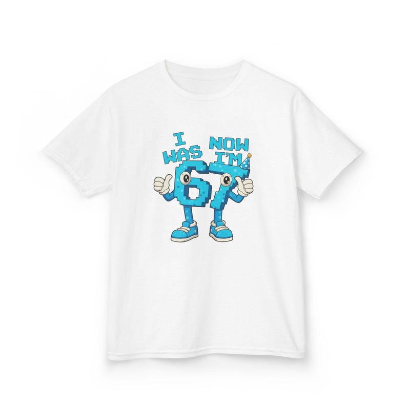 Pu&ograve; includere: T-shirt bianca con un disegno a cartoni animati del numero 67. Il numero &egrave; blu con contorni bianchi, braccia, gambe e scarpe. Il testo "I WAS 67 NOW I'M" &egrave; sopra il numero in blu. Il numero ha i pollici in su.