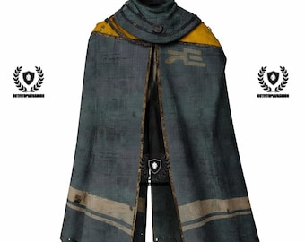 May include: A distressed-look cape in shades of teal and gray, with yellow accents on the shoulders. The cape features a high collar and a design on the front. The edges are frayed, giving it a worn appearance. The cape is likely part of a costume or cosplay.
