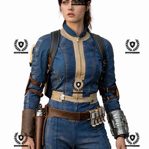 May include: A blue and tan jumpsuit with a matching jacket, belt, and accessories. The outfit includes a holster, ammunition belt, and a metallic arm guard. The jacket has a zipper and ribbed detailing.