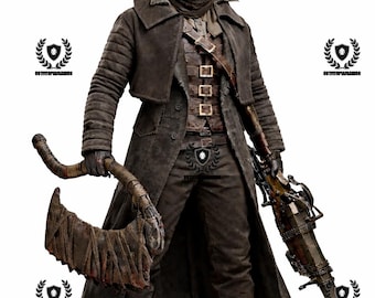 May include: A detailed statue of a character in dark brown attire, including a long coat, pants, and a mask. The figure holds a large, curved blade and a rifle-like weapon. The statue stands on a textured, circular base.