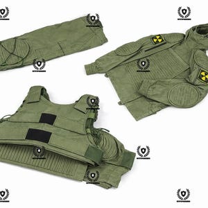 Può includere: Un completo uniforme in stile militare verde oliva, composto da pantaloni, una giacca con cappuccio e un gilet. La giacca presenta simboli di pericolo gialli sulle maniche. L'uniforme ha imbottitura rinforzata su ginocchia e gomiti.