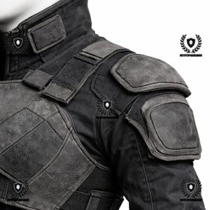 May include: Black jacket with reinforced shoulder pads and a high collar. The jacket features multiple panels and a textured, weathered appearance. The design includes a combination of smooth and padded sections, with a fitted waist and elastic band.