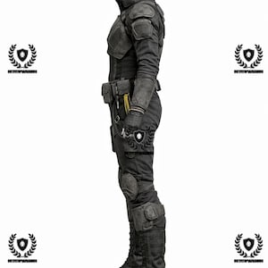 May include: A dark gray tactical suit with a high collar, shoulder pads, and knee pads. The outfit includes a belt with pouches, gloves, and tall boots. The suit is designed for protection and features a utilitarian aesthetic.