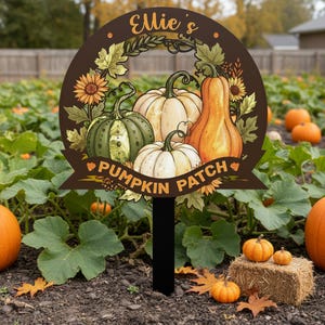 Puede incluir: Un letrero redondo marrón con el texto "Ellie's Pumpkin Patch" e ilustraciones de calabazas y girasoles. El letrero está en un jardín con calabazas y una pequeña paca de heno.
