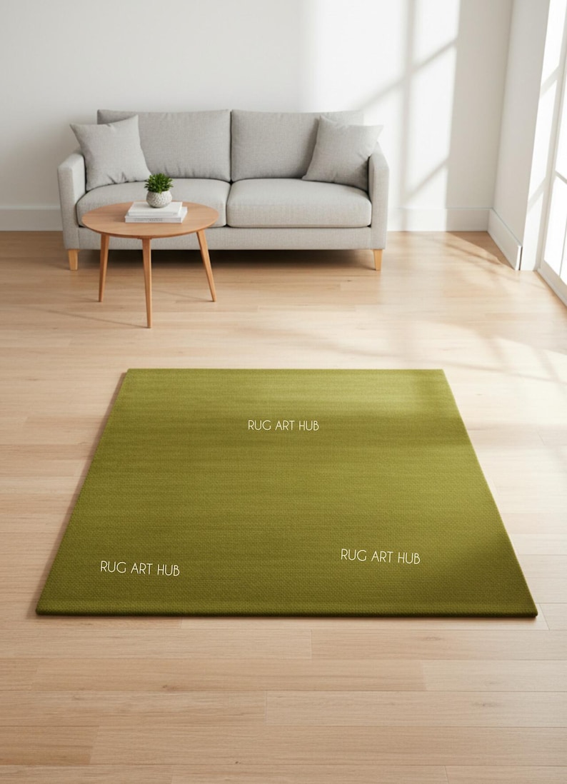 May include: A rectangular, olive green rug with a subtle gradient effect. The rug is placed on a light wood floor in a living room setting. The words "RUG ART HUB" are printed on the rug in white. A gray sofa and a wooden coffee table are in the background.