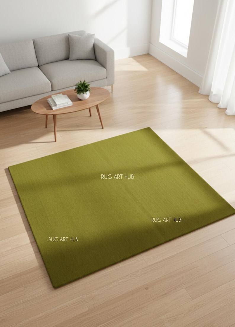 May include: A large, rectangular olive green rug with a textured surface. The rug is placed on a light wood floor in a living room setting. The words "RUG ART HUB" are printed on the rug.