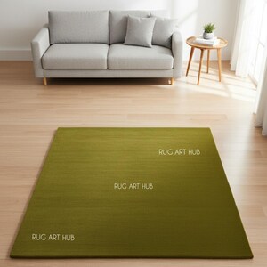 May include: A rectangular green rug with the text "RUG ART HUB" in white. The rug is placed on a hardwood floor in front of a gray sofa and a small wooden side table.