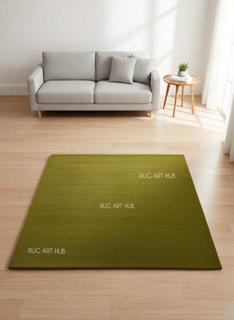 May include: A rectangular green rug with the text "RUG ART HUB" in white. The rug is placed on a hardwood floor in front of a gray sofa and a small wooden side table.