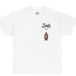 May include: White t-shirt with a crew neck. The shirt features the text "JMK" in dark gray, with "2025" below it. A brown graphic of a figure is below the text. The shirt also has the text "JMK" on the upper back.