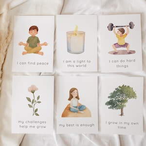 Könnte beinhalten: Set aus sechs Affirmationskarten mit Aquarellillustrationen. Jede Karte zeigt ein anderes Bild und eine positive Affirmation, darunter ein meditierendes Kind, eine Kerze und eine Person, die Gewichte hebt. Die Karten sollen Achtsamkeit und Selbstverbesserung fördern.