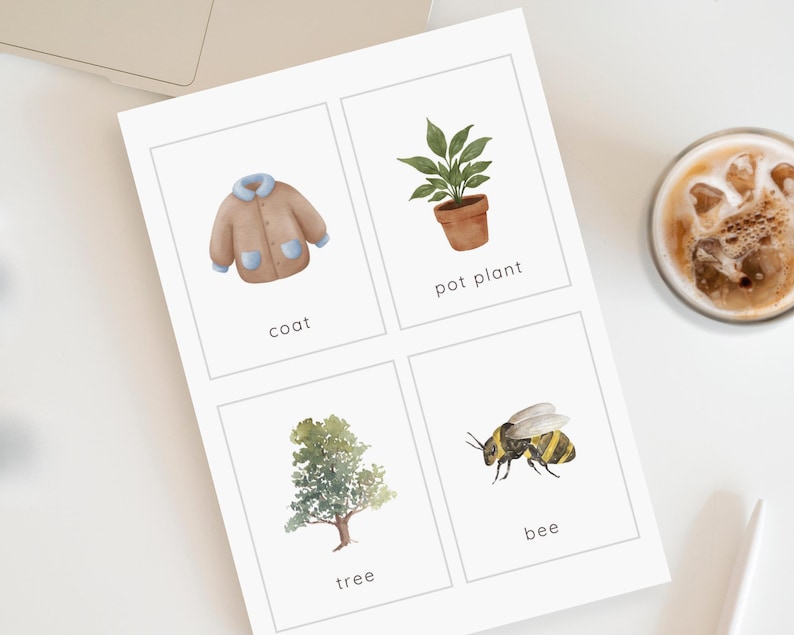 May include: A white card with four watercolor illustrations: a tan coat, a potted plant, a tree, and a bee. Each image has a corresponding word below it: "coat", "pot plant", "tree", and "bee". A cup of coffee is in the background.