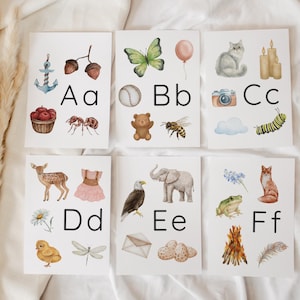 May include: Six white educational cards featuring watercolor illustrations for letters A through F. Each card displays uppercase and lowercase letters alongside various objects like an anchor, butterfly, cat, deer, elephant, and fox in soft colors.