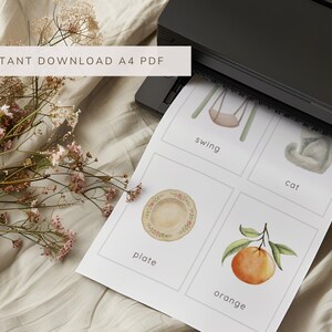May include: A4 PDF print with watercolor illustrations of a swing, cat, plate, and orange. The print is coming out of a black printer. Text at the top reads "INSTANT DOWNLOAD A4 PDF".