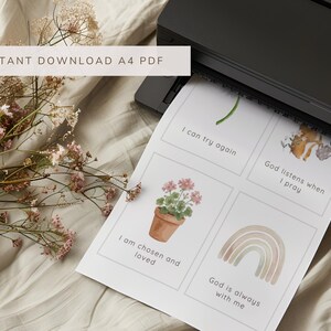 May include: A black printer outputting a white A4 sheet of paper featuring four rectangular cards with watercolor illustrations and text. The cards display a green sprout, a fox, a potted geranium, and a rainbow, with the phrases I can try again, God listens when I pray, I am chosen and loved, and God is always with me.