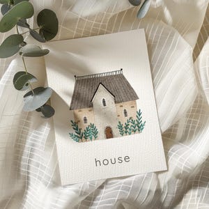 May include: Watercolor illustration of a house with a gray roof, tan walls, and a brown door. Green foliage surrounds the house. The word "house" is written in black at the bottom of the image. Eucalyptus leaves are in the upper left corner.