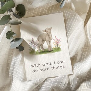 May include: A rectangular greeting card featuring a watercolor illustration of a small lamb standing in a patch of green grass with colorful wildflowers. The text "With God, I can do hard things" is printed in black below the illustration.