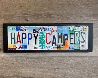 May include: A black framed sign with the words "HAPPY CAMPERS" spelled out using colorful license plates. The plates are arranged in a horizontal line and are held together with metal rivets.